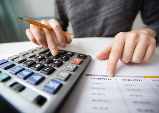 Closeup of accountant counting on calculator and working with table