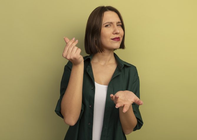 confident pretty caucasian woman holds hand open and gestures money hand sign isolated on olive green background with copy space