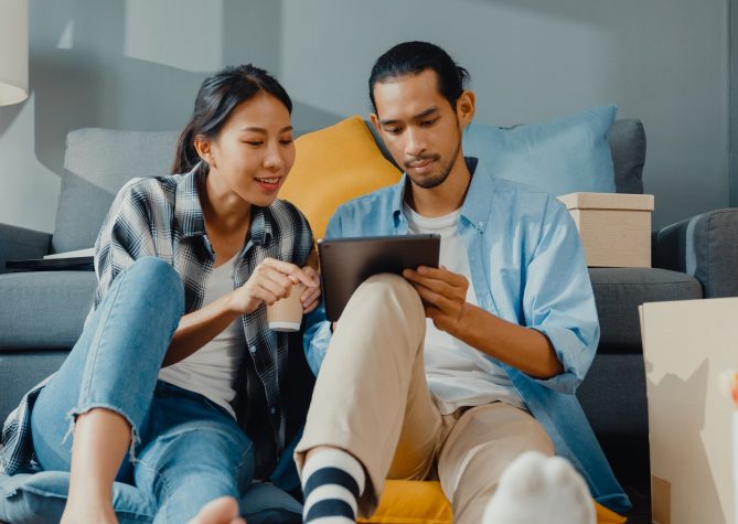 Happy asian young attractive couple man and woman use tablet online shopping furniture decorate house with carton package move in new house. Young married asian moving home shopper online concept.