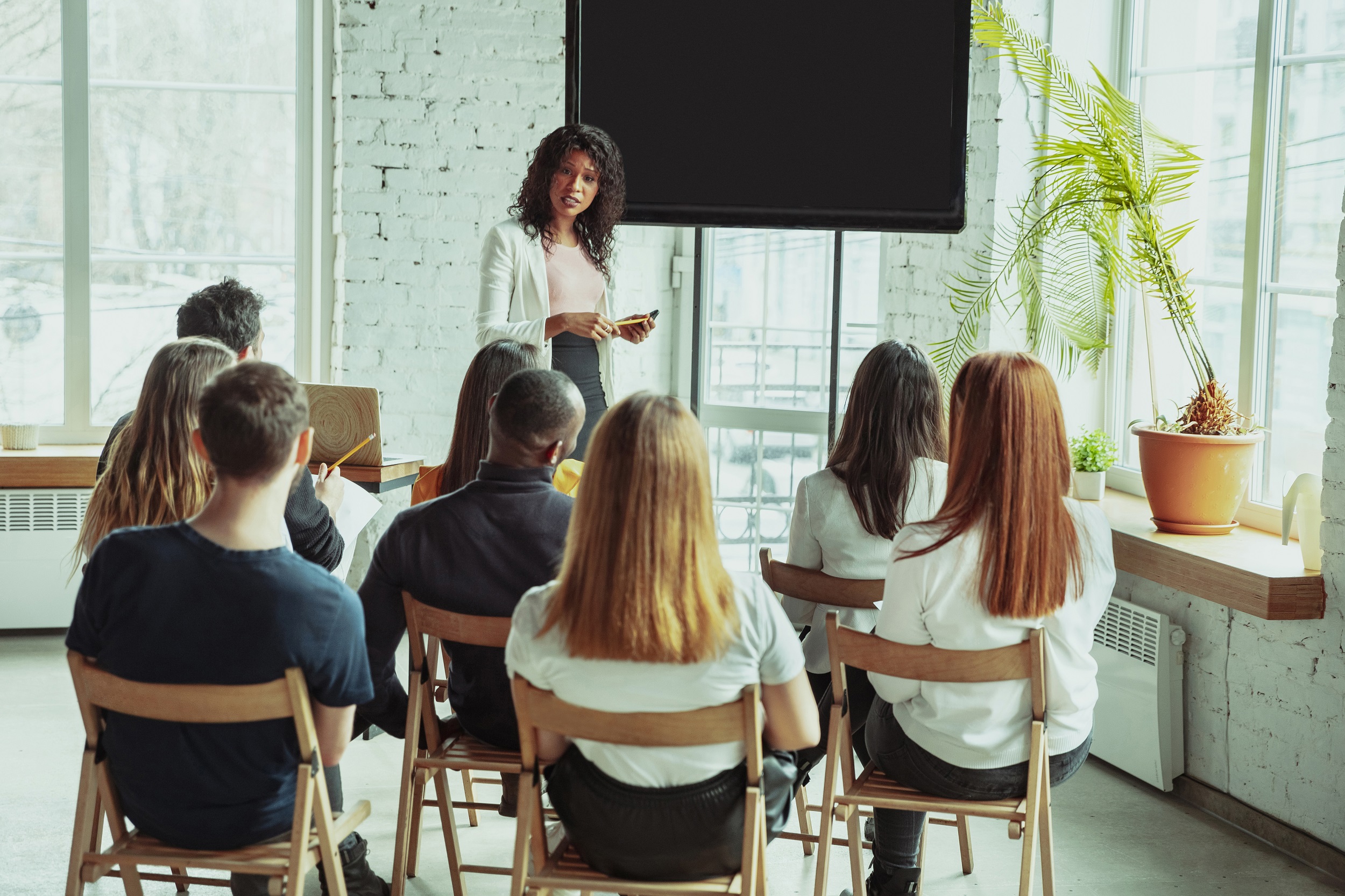 Female african-american speaker giving presentation in hall at workshop. Audience or conference hall. Rear view of participants in audience. Conference event, training. Education, diversity, inclusive concept.
