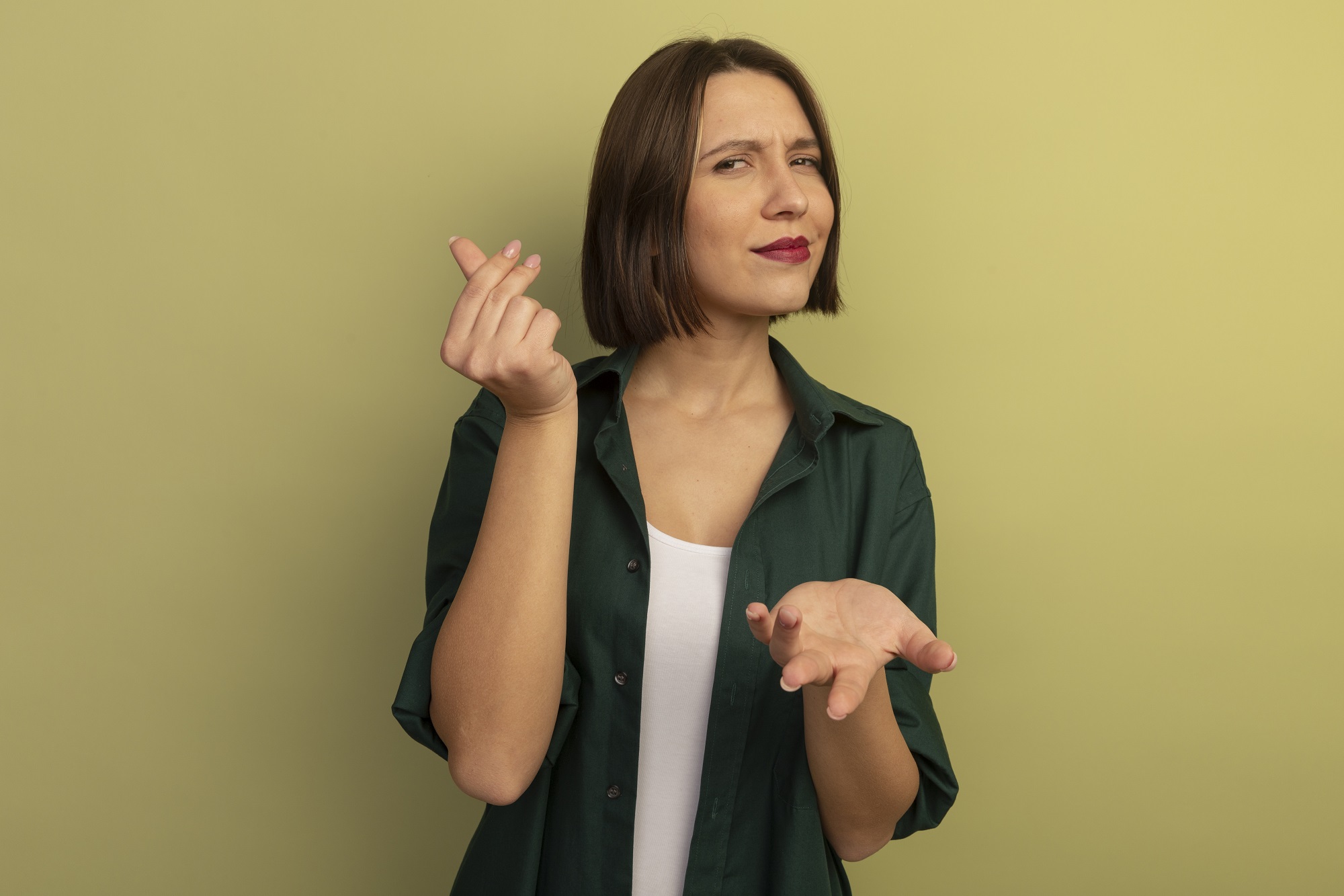 confident pretty caucasian woman holds hand open and gestures money hand sign isolated on olive green background with copy space